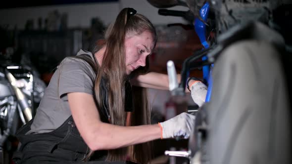 Young woman with a dirty face repairs a motorcycle in a motorcycle service