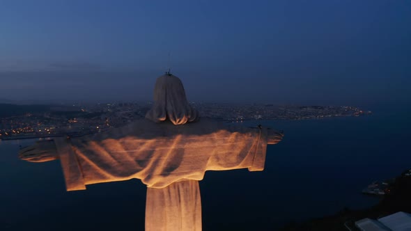 Close Up Dolly Out Aerial Night Shot of Santuario De Cristo Rei White Monument on the Hill with City