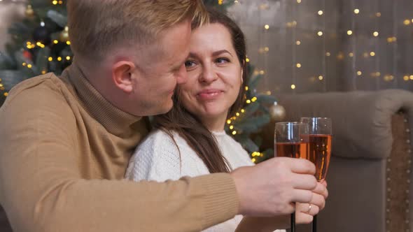 Couple in Love Sitting and Hugging Near the Christmas Tree and Drinking Champagne