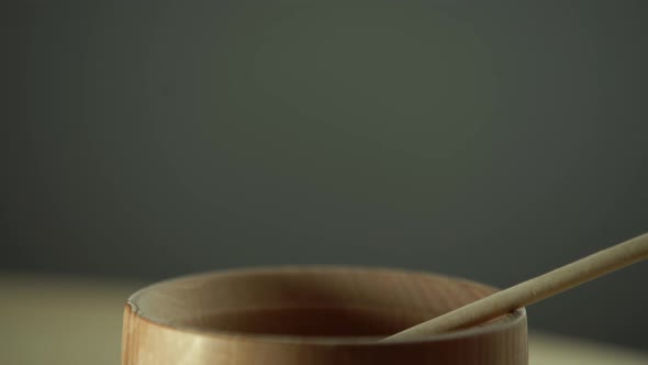 Honey with Wooden Honey Dipper in Wooden Bowl on Wooden Table