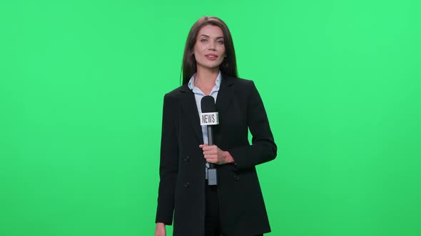 Female Reporter in Suit Looks at the Camera and Speaks Into a Microphone on a Green Background