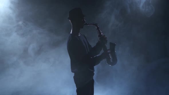 Young Jazzman Plays the Sax. Dark Smoky Studio with Spotlights