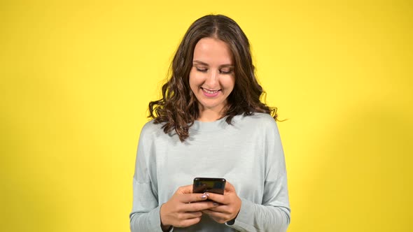 Attractive Curly Young Woman Using Smartphone Isolated on Yellow