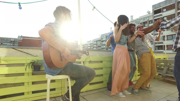 Musician playing guitar, group of people taking selfies at rooftop party