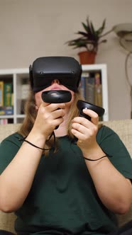 Close-up of a girl in VR glasses with controllers in her hands sitting on a couch and traveling thro