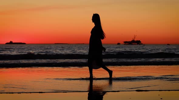 Asian woman enjoys a walk on the beach at sunset. Slow Motion.
