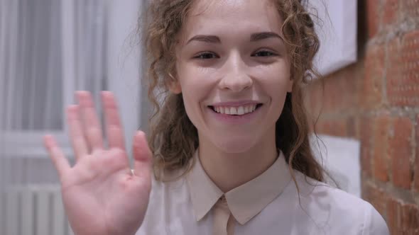 Hello By Young Female Sitting on Chair at Home Waving Hand