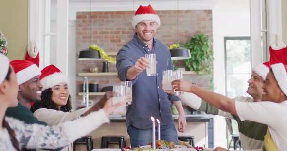 Happy group of diverse friends in santa hats celebrating meal, toasting with juice at christmas time