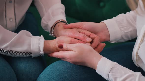 Closeup Shot of Two Women Sitting on a Dark Green Sofa Holding Hands Together Supporting Each Other