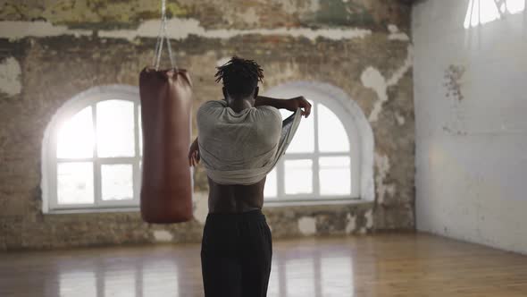 African American Athlete Walking Into Room with Boxing Pear Taking Off Shirt