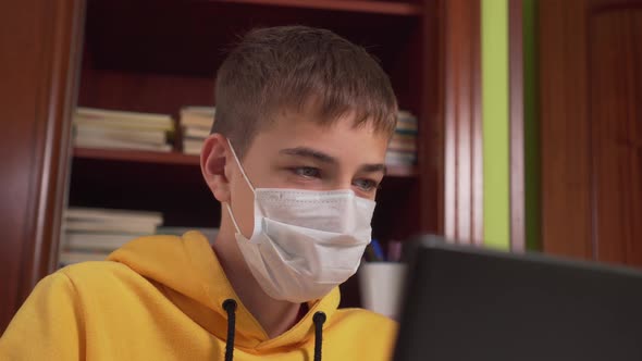 Distance learning of a teenager in a facial mask in front of a laptop at home. 