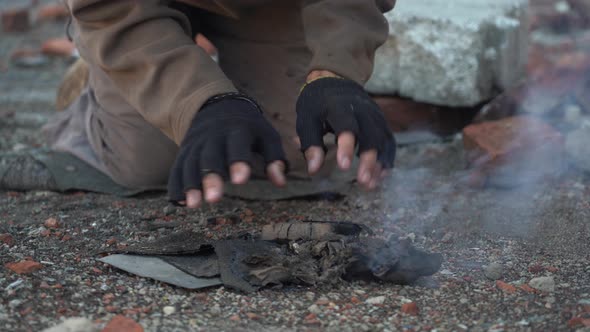 Homeless Man Warms His Hands. Hands in Black Torn Gloves Close Up. Post-apocalypse Scene