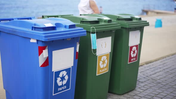 Containers for Trash Separation on Sea Beach with People Passing at Background