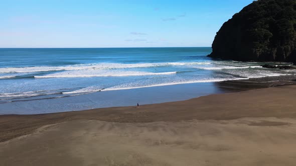 Cinematic pan of surfers walking along shoreline on Piha black sand beach in New Zealand's West coas