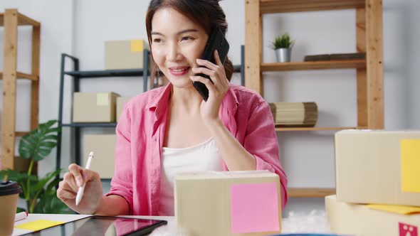 Young Asian woman using phone call receiving purchase order and check product on stock work at home.