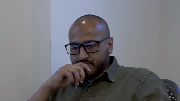 Ethnic Minority Bald Male With Eyewear, Hand On Chin, Swivelling On Chair Thinking. Static