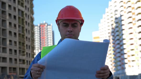 Engineer with Blueprint in Protective Helmet at Construction Site