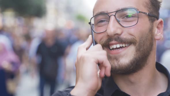 Young man talking on the phone and laughing in the crowd.