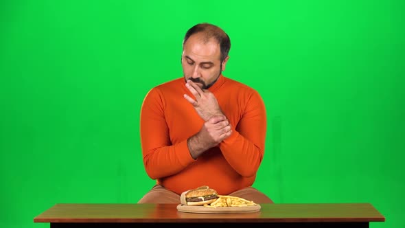 Caucasian Man with Overweight Looks at Delicious Junk Foods on the Table and Resisting Unhealthy