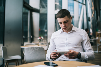 Serious man with wireless earbuds watching video on tablet