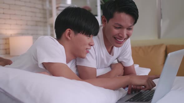 Happy gay Asian couple spending time together in bed at home.