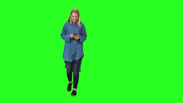 Blonde Teenager Girl Calmly Walking and Reading Text Message on Her Mobile Phone on Green Screen