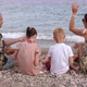 A Happy Family is Sitting on the Beach on the Seashore in the Evening on Stones - VideoHive Item for Sale
