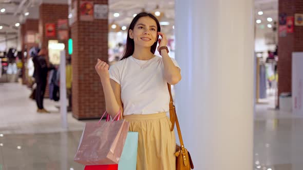 Amazed Young Woman with Paper Bags in Hand Looking at Glass Showcase in Shopping Mall