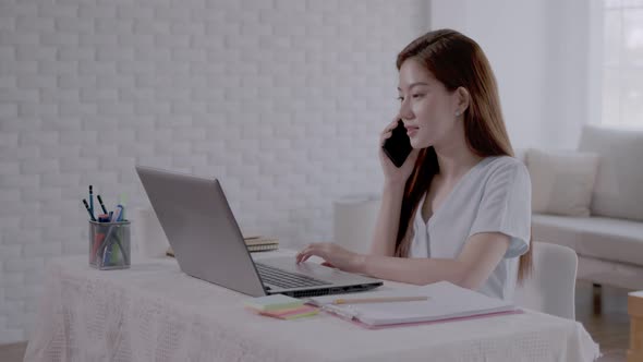 Business Asian woman Talk to work on the phone and take notes on the laptop with work from home.