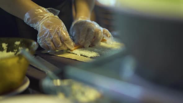 A Pair of Hands with Plastic Gloves Making Sushi Rolls on a Rustic Table Kitchen