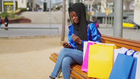 Black Shopper Adjusting Hijab and Using Smartphone