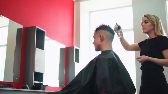 Young and Professional Hair Stylist Sprinkles Water From a Spray Gun on His Head