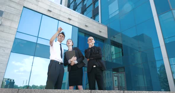 Successful Business People Discuss Business and Stand Outdoors. Two Young Men and One Woman in Suit