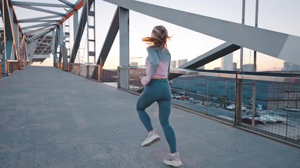 Young Slim Woman Jogging By Running Track on City Bridge