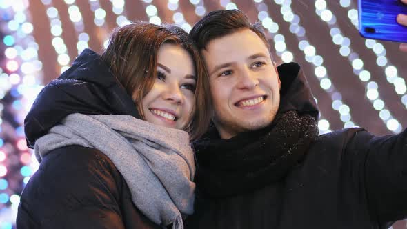 Close Up of Young Man and Woman Makes a Selfie on Phone Smiling in New Year's Night