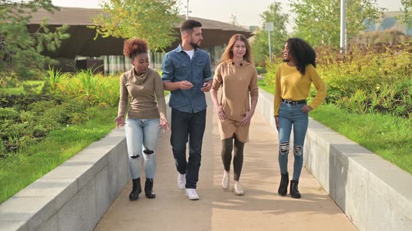 Two black women and a white man with a woman walk along the path in the park