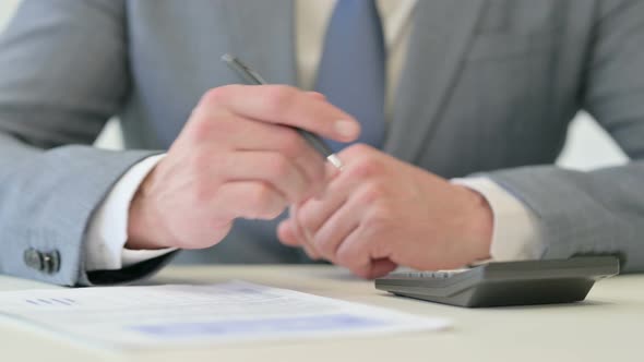 Close Up of Businessman Writing on Paper Using Calculator