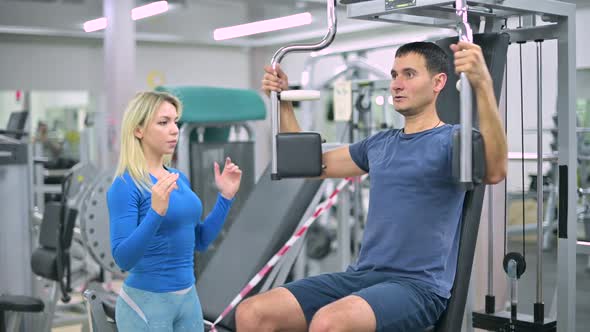 The trainer tells the client a skinny guy how to do the exercise on machine