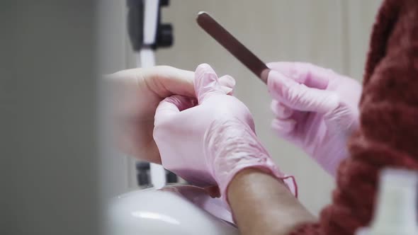 Manicurist works with client in beauty salon. Girl in pink gloves and nail file in her hands