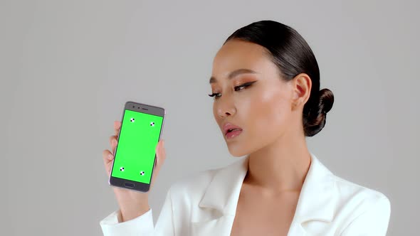 Beautiful Asian businesswoman showing smartphone with green screen