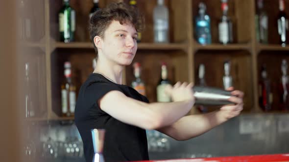 Confident Young Caucasian Bartender Shaking Cocktail Shaker in Bar Preparing Alcohol Beverage in