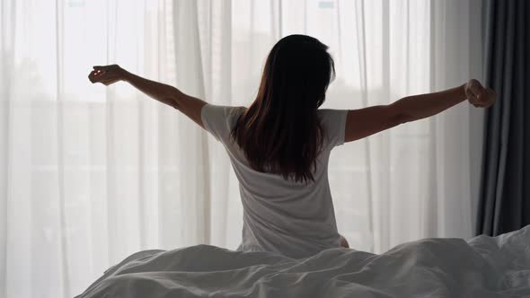 Young asian woman sitting on the bed and stretch oneself in the morning at home