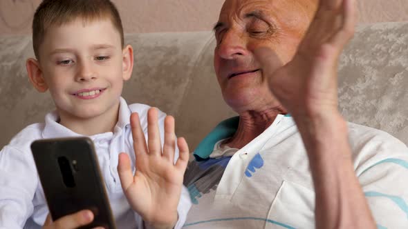 smiling caucasian boy 7 years old with grandfather 70 years old waving hand in front of phone screen