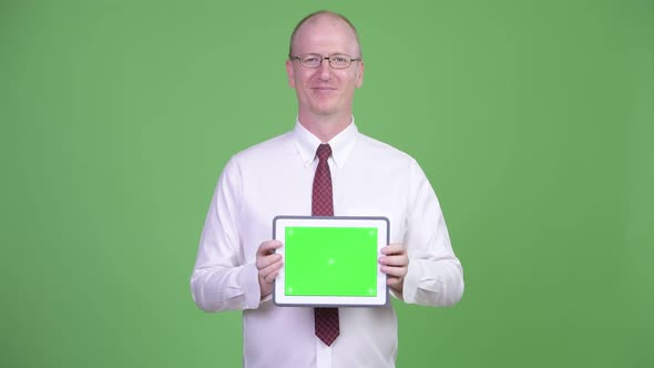 Happy Mature Bald Businessman Showing Digital Tablet