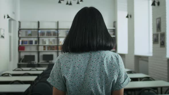 Happy Woman Reads a Book in the Library Chooses Books From the Shelf alt