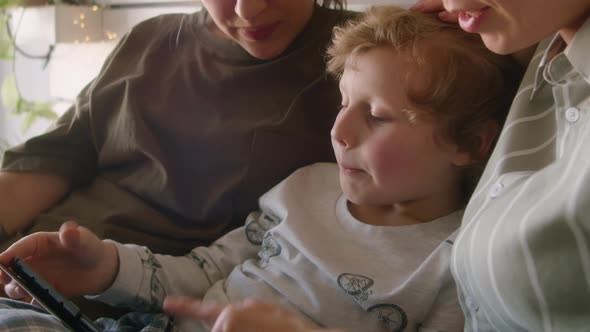 Little Boy Using Tablet and Chatting with Lesbian Mothers on Bed