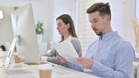 Creative Man Reading Documents and Working on Desktop