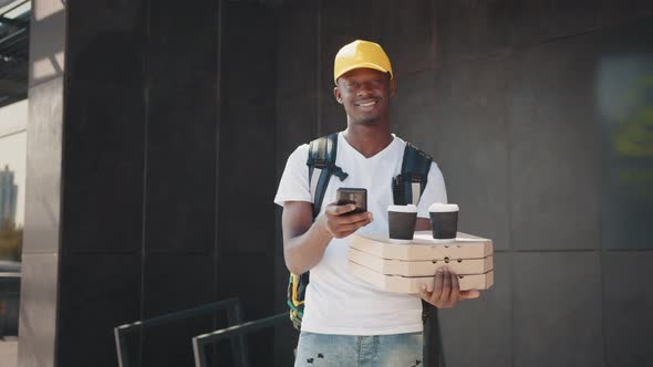 Portrait of African Courier with Package and Smartphone Carrying Box of Pizza