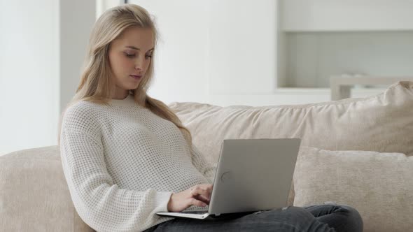 Pregnant Woman is Sitting on a Beige Sofa with a Laptop