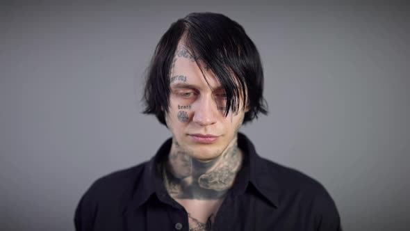 Closeup Frustrated Tattooed Young Man Standing at Grey Background and Looking at Camera